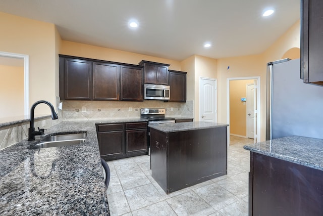 kitchen featuring appliances with stainless steel finishes, dark stone countertops, sink, dark brown cabinetry, and a center island