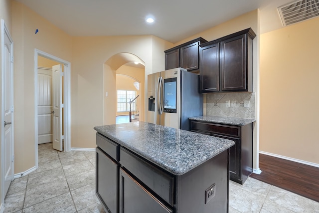 kitchen with backsplash, a center island, dark brown cabinetry, dark stone counters, and stainless steel refrigerator with ice dispenser