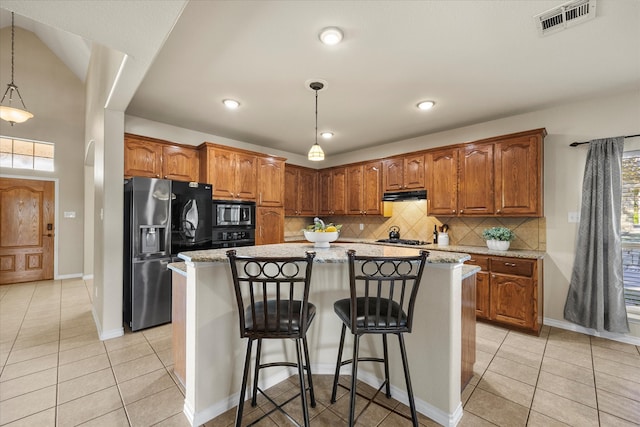 kitchen with appliances with stainless steel finishes, light stone counters, a breakfast bar, decorative light fixtures, and a kitchen island