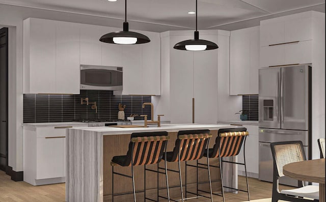 kitchen featuring white cabinets, a center island with sink, hanging light fixtures, light hardwood / wood-style floors, and stainless steel appliances