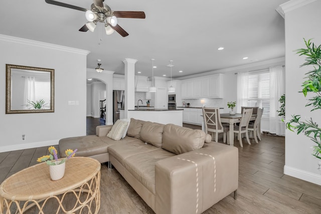 living room with crown molding, sink, ceiling fan, and light wood-type flooring