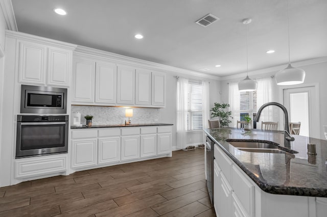 kitchen featuring appliances with stainless steel finishes, dark hardwood / wood-style flooring, dark stone counters, crown molding, and sink