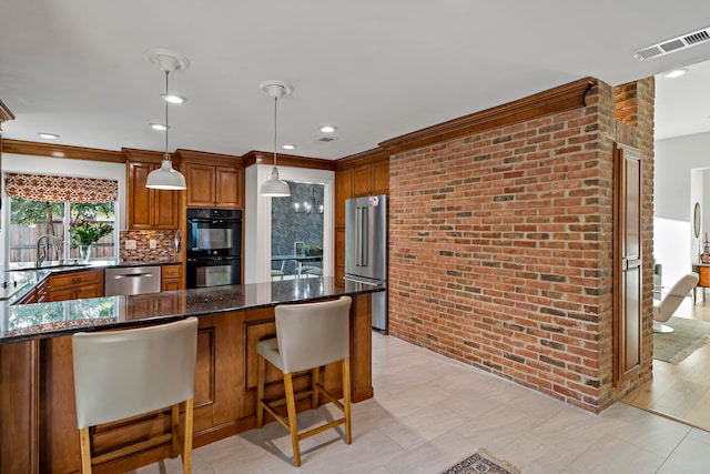 kitchen with a breakfast bar area, appliances with stainless steel finishes, dark stone counters, pendant lighting, and crown molding