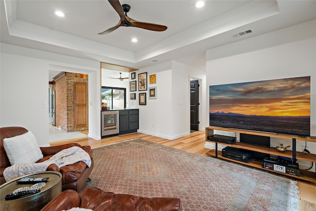 living room featuring crown molding, wine cooler, light wood-type flooring, and a raised ceiling