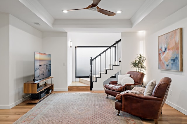 living area featuring crown molding, ceiling fan, wood-type flooring, and a raised ceiling