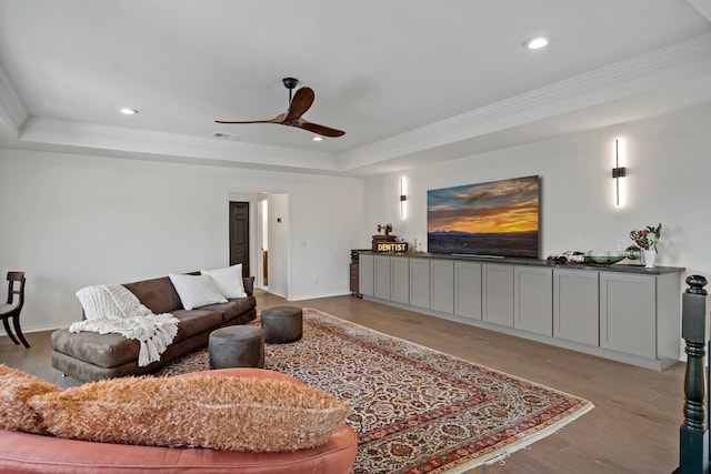 living room featuring ornamental molding, a tray ceiling, light wood-type flooring, and ceiling fan