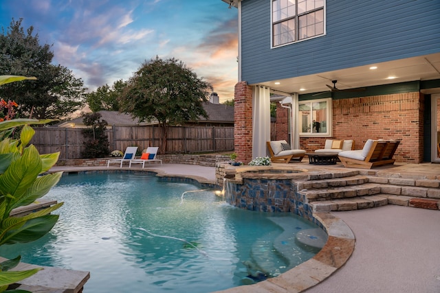 pool at dusk featuring an in ground hot tub, pool water feature, a fire pit, a patio, and ceiling fan