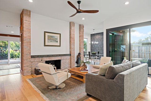 living room featuring ceiling fan, decorative columns, light hardwood / wood-style flooring, and a fireplace