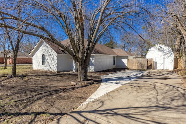 view of front of house with an outbuilding, a storage shed, brick siding, fence, and driveway