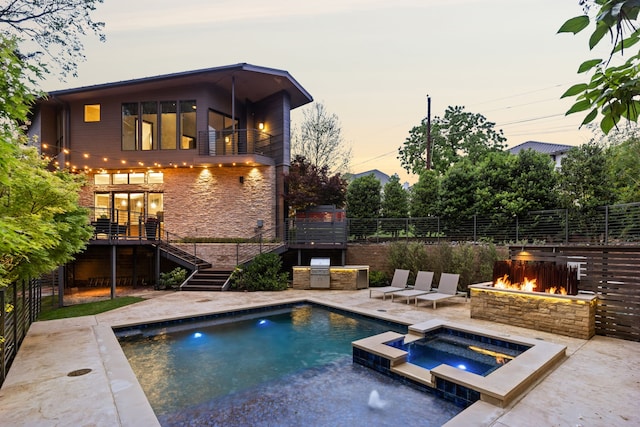 pool at dusk featuring an in ground hot tub, exterior kitchen, a patio area, and a fire pit