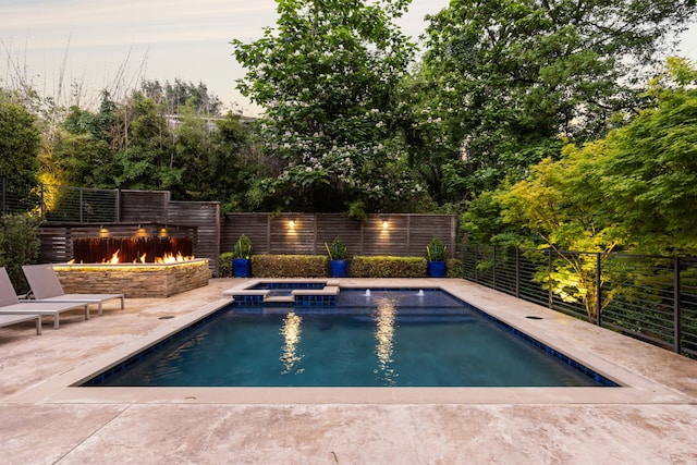 pool at dusk with a patio and an in ground hot tub