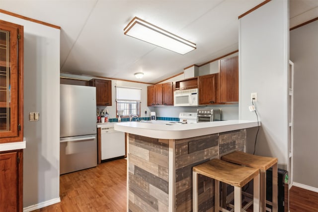 kitchen with white appliances, light wood-type flooring, kitchen peninsula, vaulted ceiling, and a breakfast bar area