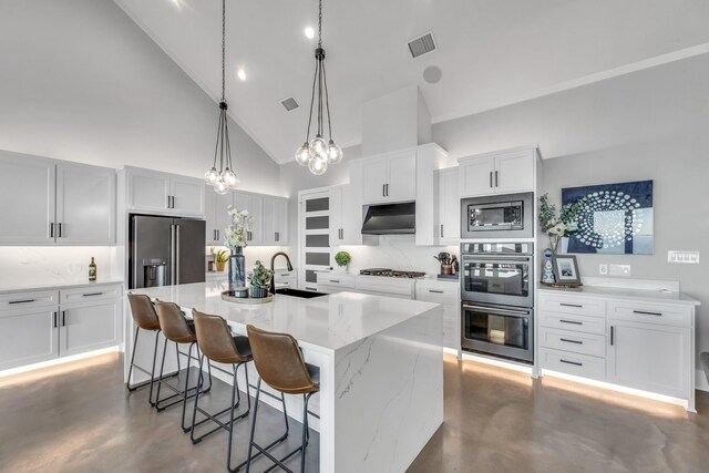 kitchen featuring appliances with stainless steel finishes, high vaulted ceiling, white cabinetry, a breakfast bar area, and an island with sink