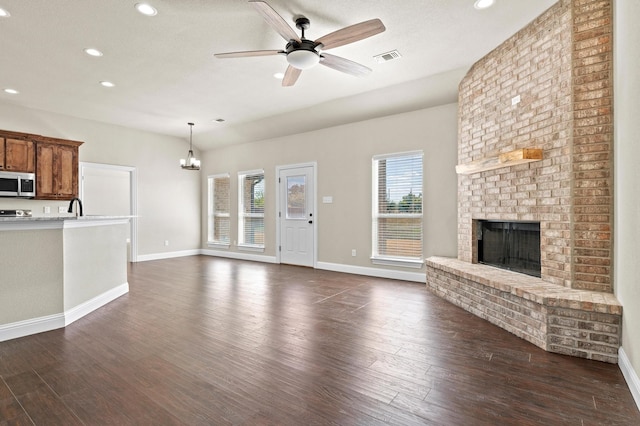 unfurnished living room featuring ceiling fan with notable chandelier, a fireplace, sink, and dark hardwood / wood-style floors