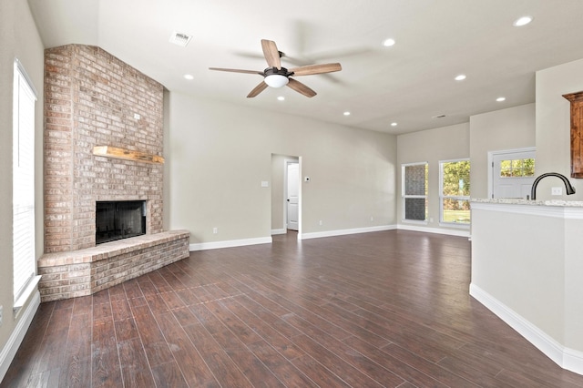 unfurnished living room featuring sink, a brick fireplace, dark hardwood / wood-style floors, and ceiling fan