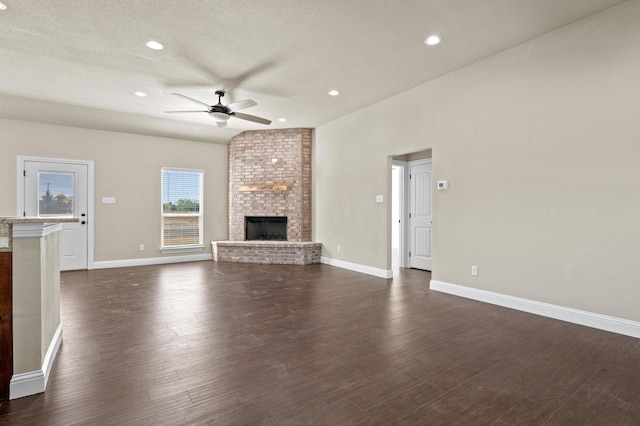 unfurnished living room with dark wood-type flooring, a brick fireplace, a textured ceiling, and ceiling fan