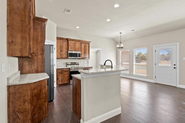 kitchen featuring appliances with stainless steel finishes, dark hardwood / wood-style floors, hanging light fixtures, and an island with sink