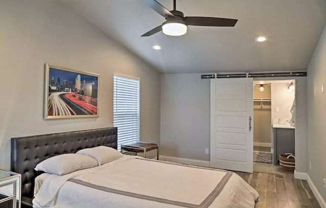 bedroom featuring lofted ceiling, a walk in closet, hardwood / wood-style floors, a barn door, and ceiling fan