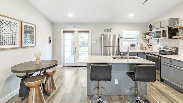 kitchen with appliances with stainless steel finishes, gray cabinetry, a healthy amount of sunlight, and an island with sink