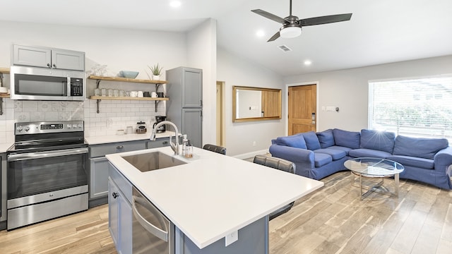 kitchen with stainless steel appliances, a center island with sink, sink, vaulted ceiling, and gray cabinets