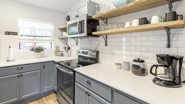 kitchen with gray cabinetry, backsplash, appliances with stainless steel finishes, and light wood-type flooring