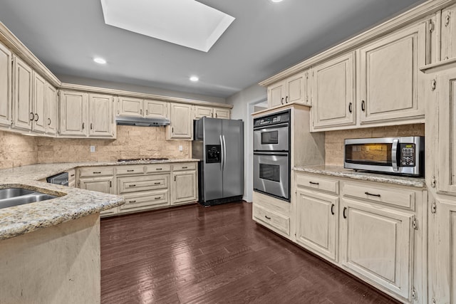 kitchen featuring decorative backsplash, dark hardwood / wood-style flooring, appliances with stainless steel finishes, light stone countertops, and a skylight