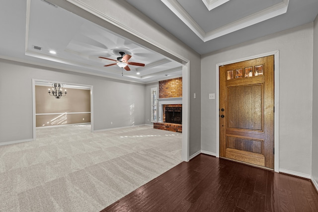 entrance foyer with a tray ceiling, wood-type flooring, ornamental molding, a fireplace, and ceiling fan with notable chandelier