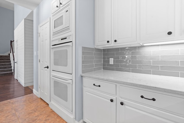 kitchen featuring tasteful backsplash, light tile patterned floors, white cabinetry, light stone counters, and white appliances