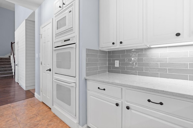 kitchen with white cabinetry, light stone countertops, white appliances, and decorative backsplash