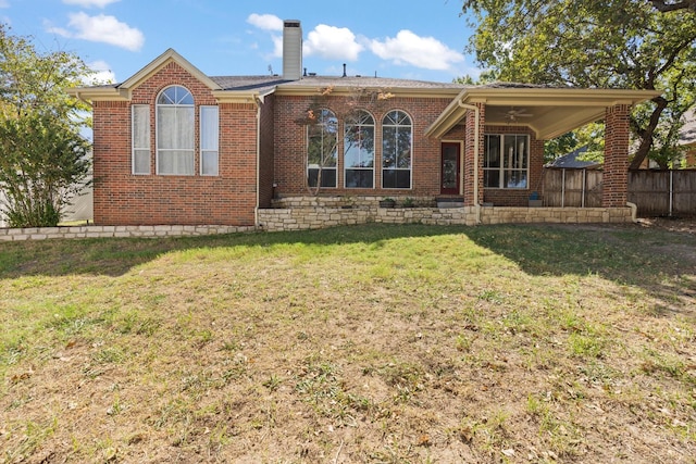 rear view of property featuring a chimney, brick siding, fence, and a lawn