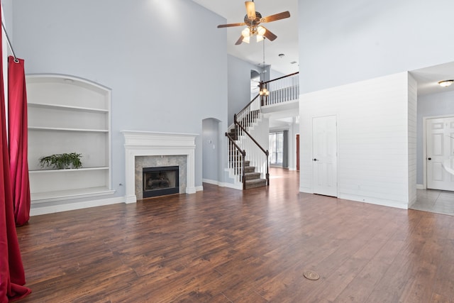 unfurnished living room featuring dark hardwood / wood-style floors, ceiling fan, a high ceiling, and built in shelves