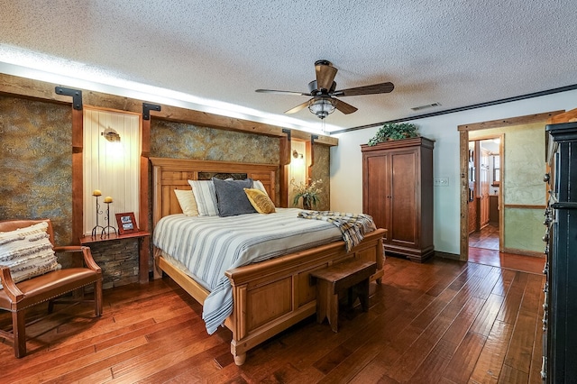 bedroom with a textured ceiling, a barn door, dark hardwood / wood-style floors, and ceiling fan