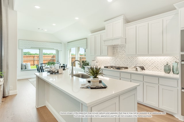 kitchen with white cabinetry, light hardwood / wood-style floors, sink, and a center island with sink