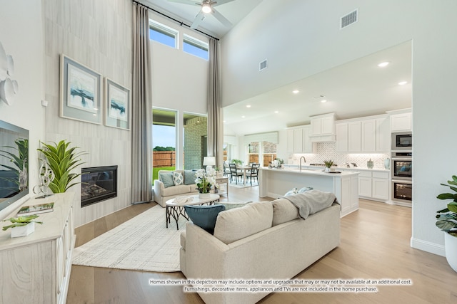 living room featuring a towering ceiling, light hardwood / wood-style flooring, sink, and a fireplace