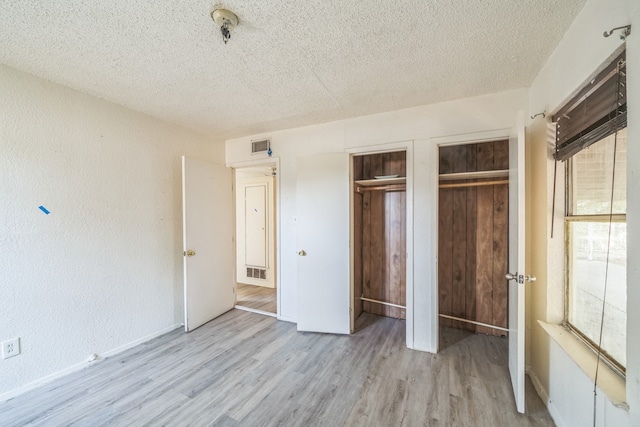 unfurnished bedroom with a textured ceiling, multiple closets, and light wood-type flooring