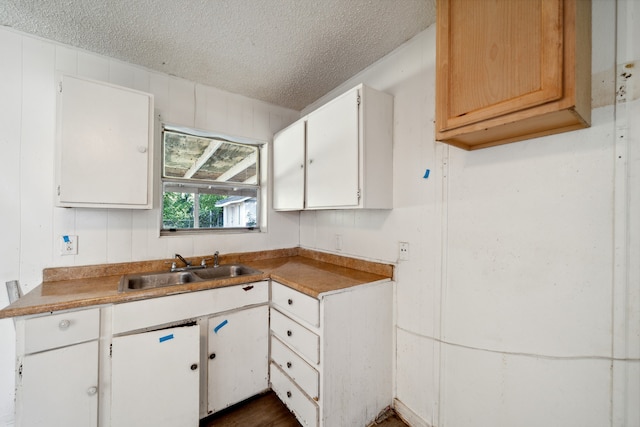 kitchen featuring a textured ceiling, sink, wooden walls, and white cabinets