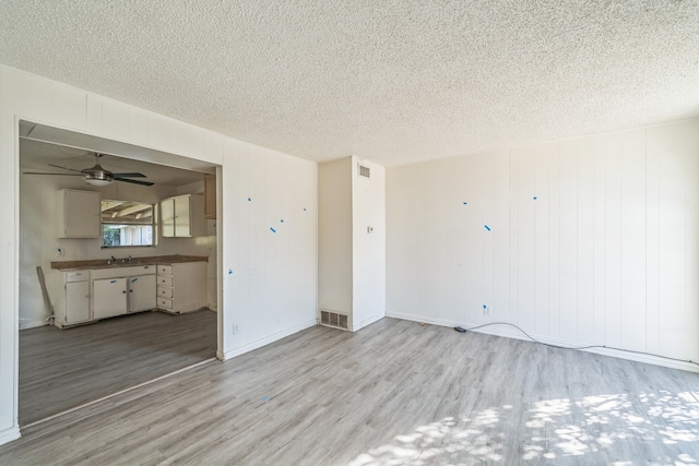 unfurnished room featuring light hardwood / wood-style flooring, a textured ceiling, sink, and ceiling fan