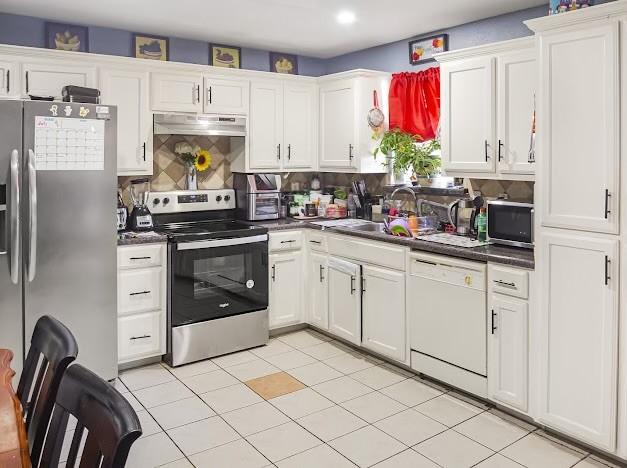 kitchen with appliances with stainless steel finishes, a sink, dark countertops, white cabinetry, and recessed lighting
