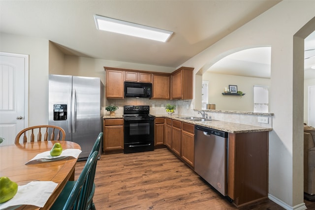 kitchen featuring tasteful backsplash, black appliances, dark wood-type flooring, sink, and light stone counters