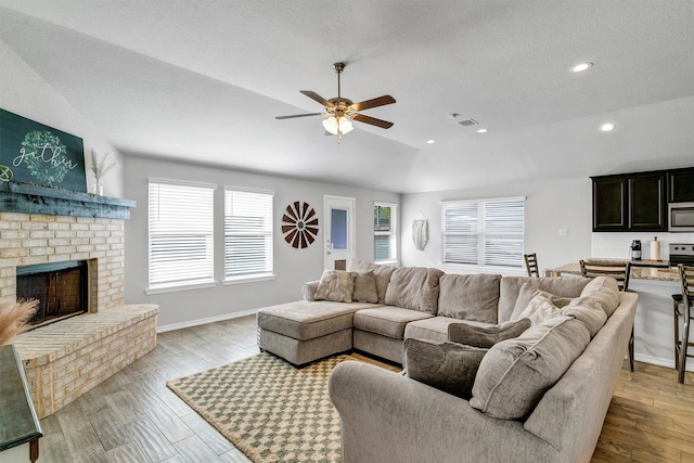 living room with light hardwood / wood-style flooring, ceiling fan, a brick fireplace, and plenty of natural light