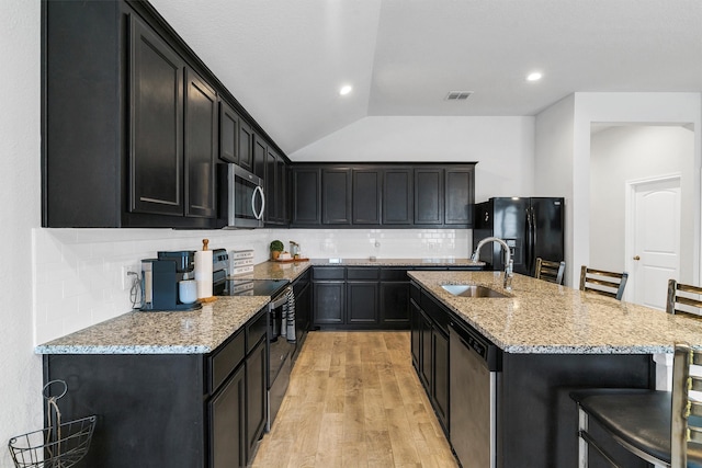 kitchen with a kitchen bar, stainless steel appliances, lofted ceiling, light hardwood / wood-style floors, and decorative backsplash