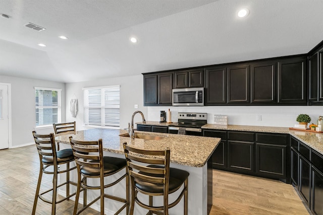 kitchen featuring stainless steel appliances, sink, a breakfast bar, an island with sink, and light wood-type flooring