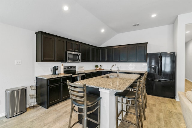 kitchen with light hardwood / wood-style flooring, lofted ceiling, a center island with sink, and stainless steel appliances