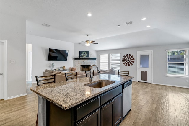 kitchen featuring light stone counters, sink, light hardwood / wood-style floors, dishwasher, and a kitchen island with sink