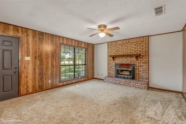 unfurnished living room featuring carpet, a brick fireplace, ceiling fan, a textured ceiling, and wood walls