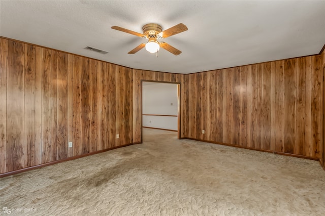 empty room featuring light carpet, wooden walls, and ceiling fan