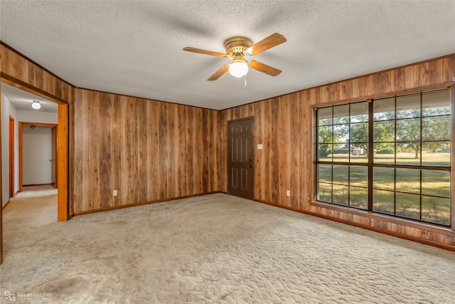 carpeted spare room featuring ceiling fan, a textured ceiling, and wooden walls