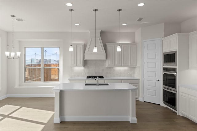 kitchen featuring white cabinetry, decorative light fixtures, an island with sink, and tasteful backsplash