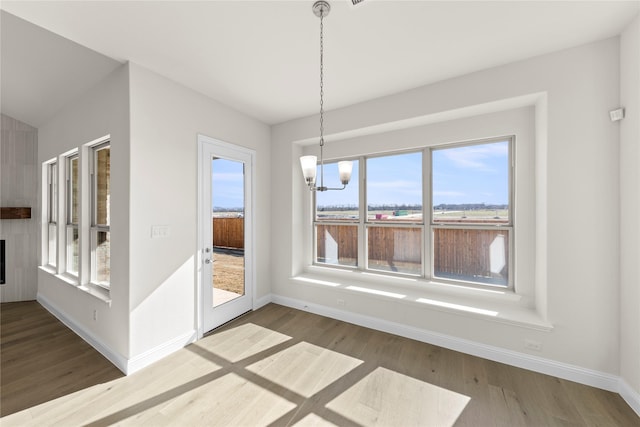 unfurnished dining area with a healthy amount of sunlight, hardwood / wood-style floors, and an inviting chandelier