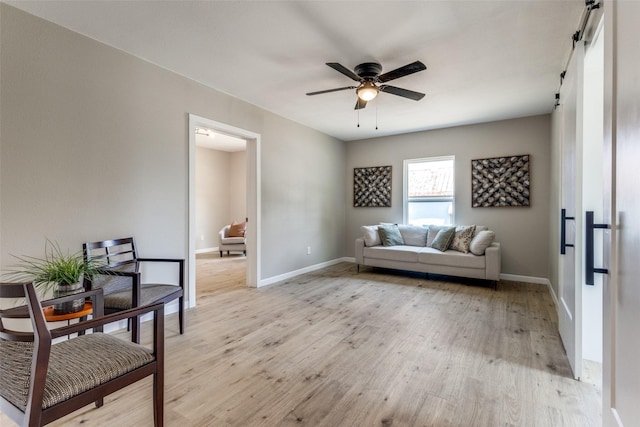 living area with light wood-type flooring, ceiling fan, and a barn door